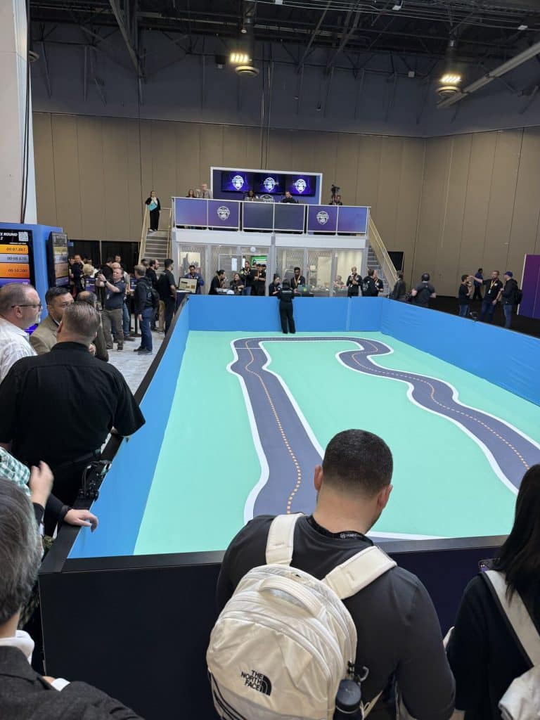 Attendees gathered around the AWS DeepRacer track at AWS re:Invent 2024, observing autonomous racing cars.