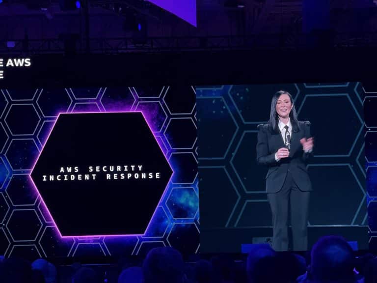 Speaker presenting AWS Security Incident Response session at AWS re:Invent 2024 on a stage with a hexagonal-themed backdrop.