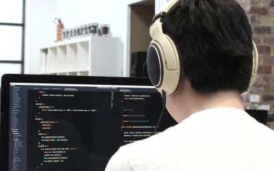 A developer with headphones on, working on coding and customization on a computer screen in a modern office setting.