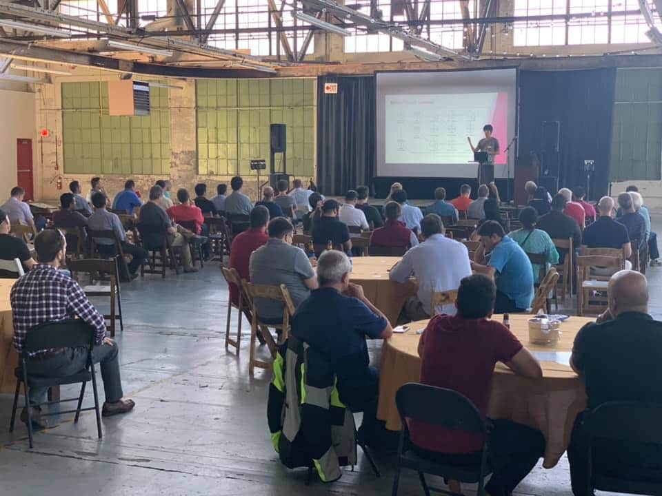Attendees at PTP's first New England AWS Innovation Expo and Summer BBQ event listen to a presentation in an industrial-style venue.