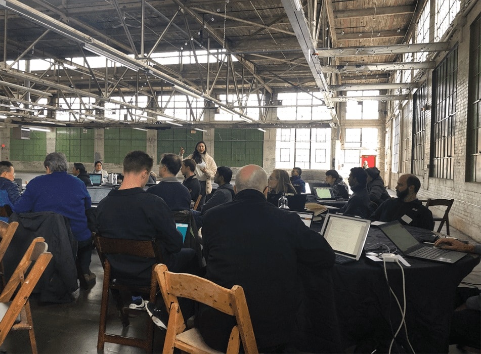 Photo of a training session at the AWS DeepRacer event with participants working on laptops in a rustic industrial setting.