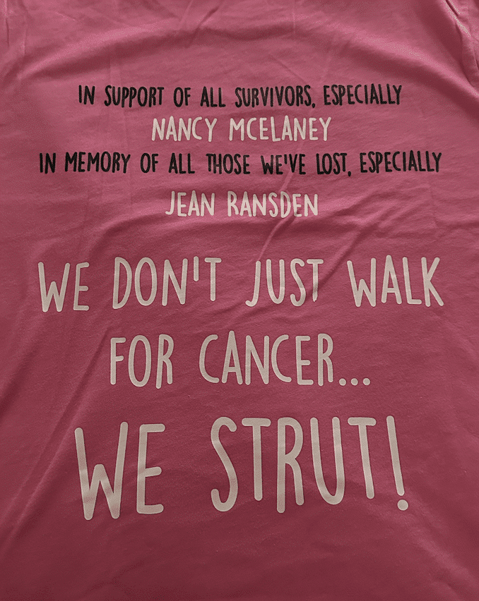 Photo of the event T-shirt in pink with white lettering that reads, 'In support of all survivors, especially Nancy McElaney. In memory of all those we've lost, especially Jean Ransden. We don't just walk for cancer...we strut!